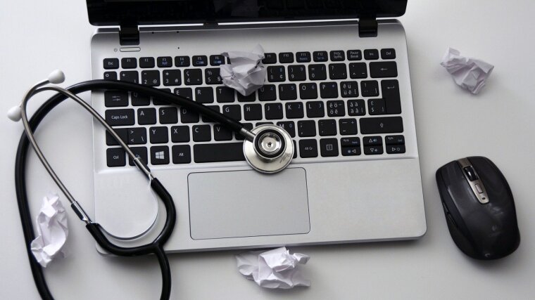 Ein aufgeklappter Laptop mit Maus, Stethoskop und zusammengeknülltem Papier